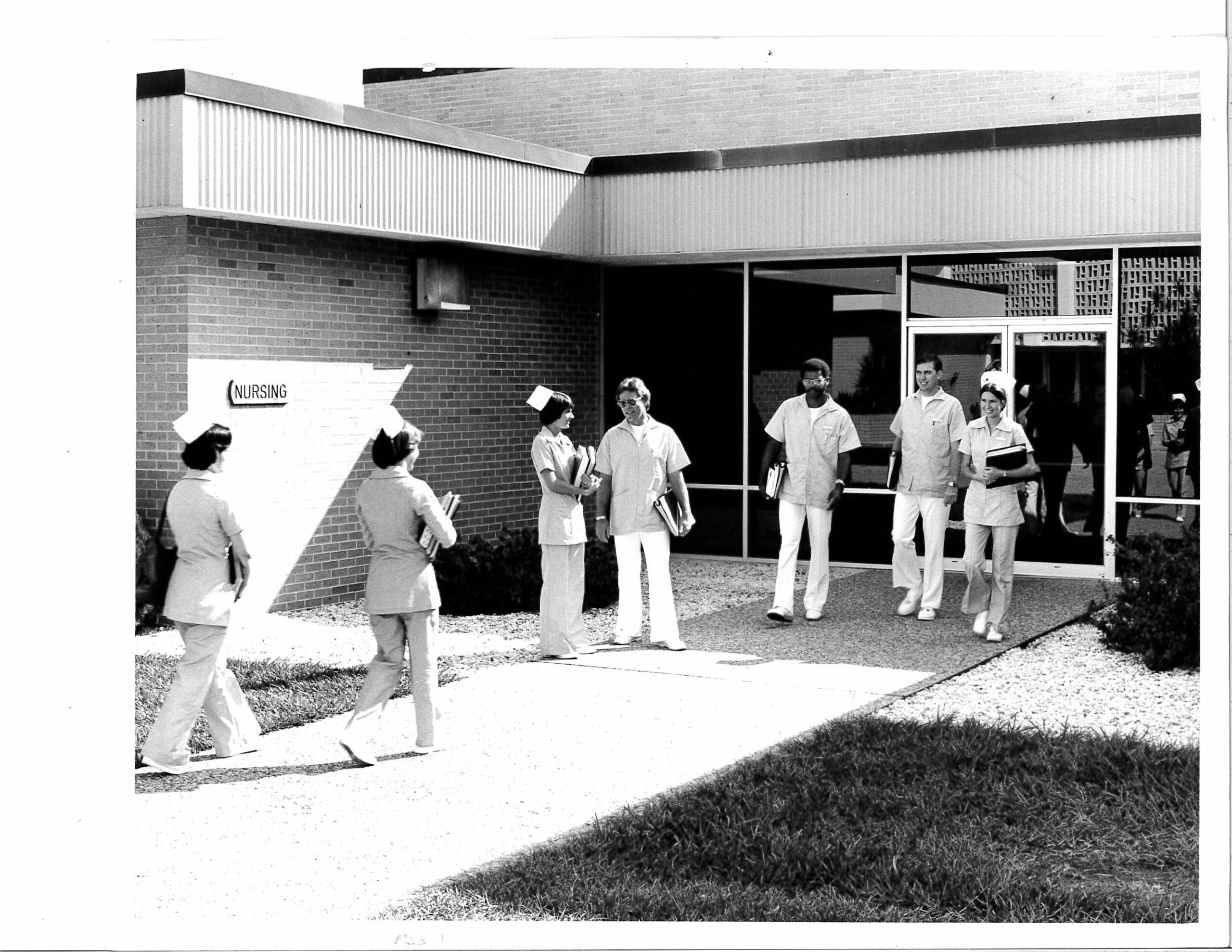 A group of diverse nursing students mingle outside of a nurse training building.