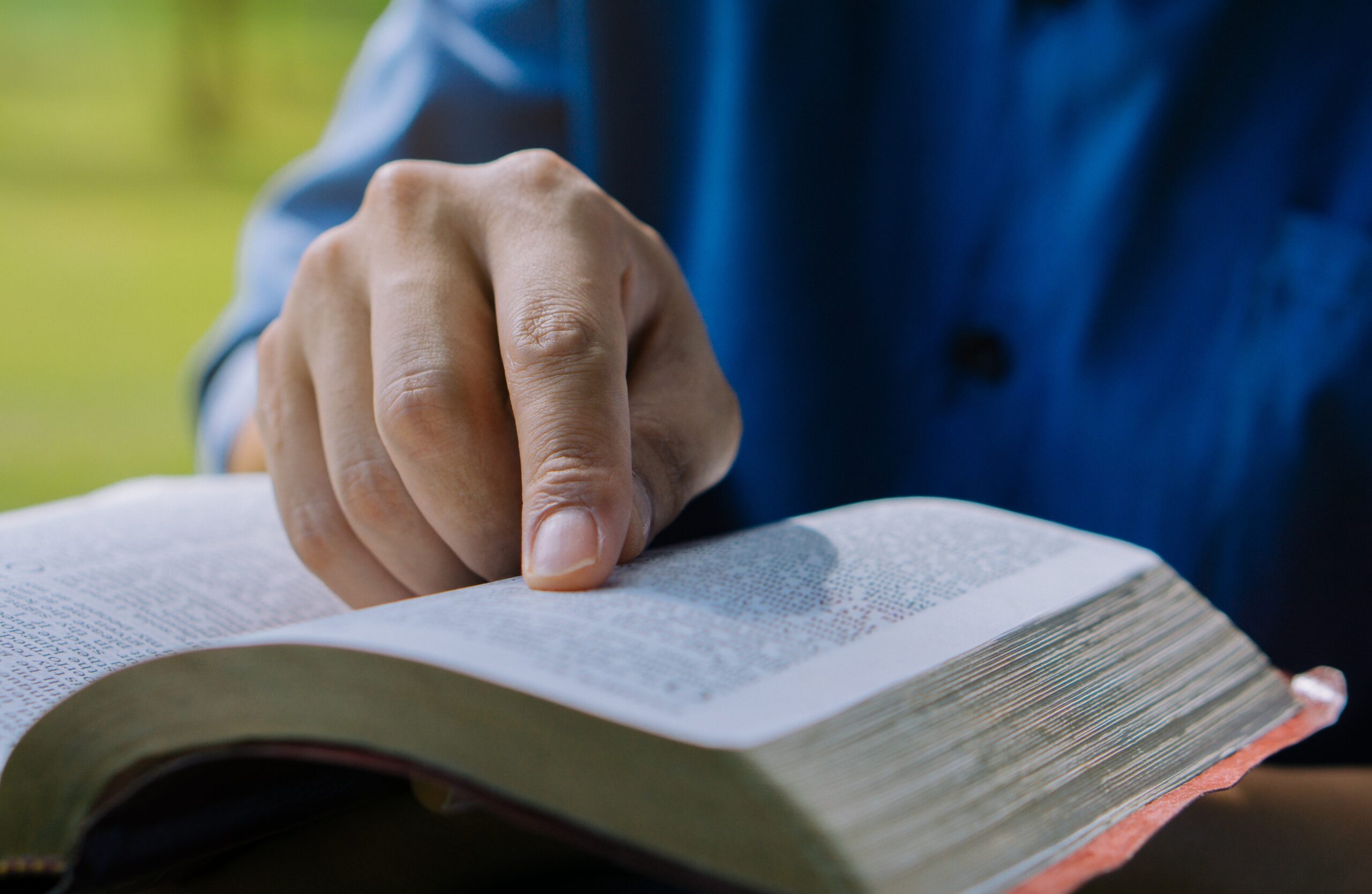 A person in a blue shirt points to a page in a book.